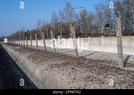 Graben und elektrischer Stacheldrahtzaun in der Nähe eines Wachturms, um Gefangene vor der Flucht im Konzentrationslager Dachau zu bewahren Stockfoto