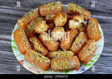 Tulumba, Bamiyeh oder Balah El Sham gefüllt mit Schlagsahne und bedeckt mit Pistazien und Nüssen, frittiertem Teig Dessert getränkt in Sirup, ähnliches Stockfoto