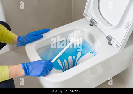 Wandmontierte Toilettenreinigung. Das Zimmermädchen reinigt die Toilette mit einer Bürste. Frauenhaushaltsdienst Stockfoto
