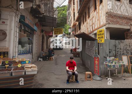 Bild eines jungen Mannes, der vor einer Straße in Istanbul in der Türkei sitzt und sein Handy, ein Smartphone, benutzt, um im Internet zu surfen. Stockfoto