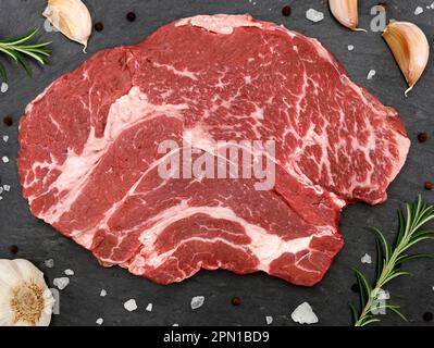Draufsicht auf ein rohes Rindersteak mit Kräutern, Gewürzen und Knoblauch auf einem Schiefertafel Stockfoto