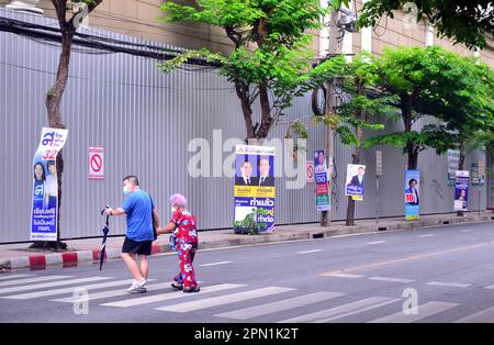 Ein Mann hilft einer älteren Frau über die Surawong Road. Wahlkandidaten verwenden Plakate an Straßenmöbeln, um sich bei potenziellen Wählern im Silom District, im Zentrum von Bangkok, Thailand und Südostasien zu bewerben. Nach der Auflösung des 25. Repräsentantenhauses am 20. März 2023 werden in Thailand am 14. Mai 2023 allgemeine Wahlen stattfinden. Stockfoto