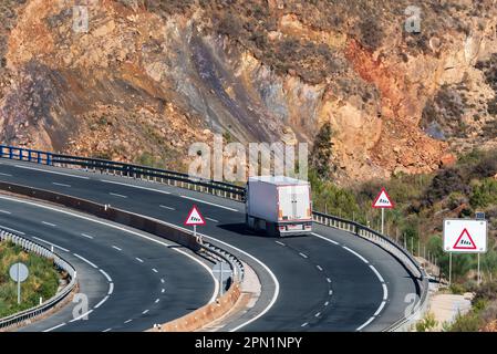 LKW mit einem gekühlten Auflieger, der auf der Straße fährt, mit Warnschildern für starken Wind. Stockfoto