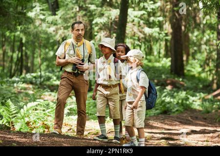 Panoramaaussicht bei einer vielfältigen Gruppe von Spähern, die im Wald wandern, mit einem Erwachsenen, einem Führer, Kopierraum Stockfoto