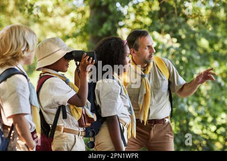 Seitlicher Blick auf eine vielfältige Gruppe von Spähern im Wald, die die Natur erkunden und in Ferngläsern schauen Stockfoto