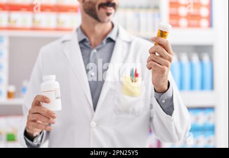 Junger hispanic-Mann Apotheker hält Pillen Flaschen in der Apotheke Stockfoto