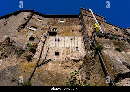 Ehrwürdige Häuser mit geflickten Schutt-Wänden, langen Abflussrohren und ausgetauschten Fenstern scheinen aus vulkanischen Felsen auf einem Hügel in Bomarzo, Latium, Italien, zu wachsen. Sie stehen neben dem Palazzo Orsini, einem großen Renaissance-Herzogspalast, der von 1500s pensioniertem Militärführer und Kunstpatron Vicino Orsini (1523-1583) geschaffen wurde. Stockfoto