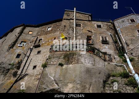 Traditionelle Hochhäuser mit verflickten Steinmauern und ausgetauschten Fenstern teilen sich einen vulkanischen Hügel in Bomarzo, Latium, Italien, mit dem Palazzo Orsini, einem großen Renaissance-Herzogspalast, der in den 1500s Jahren für die wohlhabende Familie Orsini gebaut wurde. Der Palast wurde hauptsächlich von Pier Francesco Orsini erbaut, einem pensionierten Militärbefehlshaber und Kunstpatron, der zu seinen Lebzeiten als Vicino Orsini bekannt war. Stockfoto