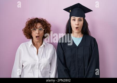 Hispanische Mutter und Tochter, die eine Abschlussmütze und einen Morgenmantel trugen, ängstlich und schockiert mit Überraschungsausdruck, Angst und aufgeregtem Gesicht. Stockfoto