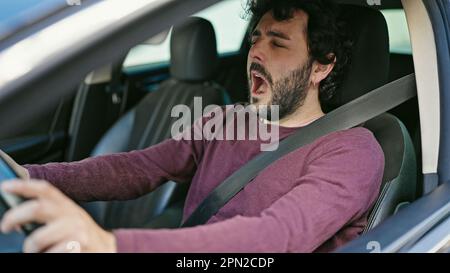 Ein junger latino, der ein Auto fährt, gähnt auf der Straße Stockfoto