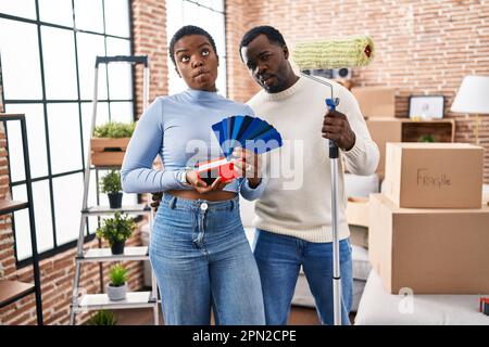 Ein junges afroamerikanisches Paar zieht in ein neues Haus und wählt die Farbe der Wände, das Fischgesicht mit Mund und schielenden Augen macht, verrückt und komisch. Stockfoto