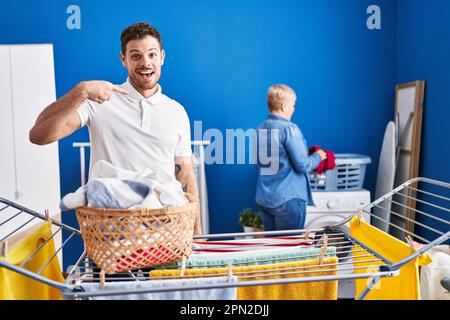 Hispanische Mutter und Sohn hängen Kleider an der Wäscheleine zeigen Finger auf ein selbst lächeln glücklich und stolz Stockfoto
