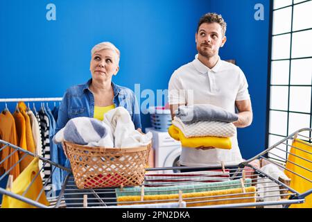 Hispanische Mutter und Sohn hängen Kleider an der Wäscheleine, lächeln zur Seite und starren weg, denken. Stockfoto