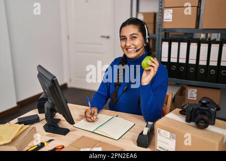Junge hispanische Frau E-Commerce Call Center Agent mit Videoanruf halten Apfel im Büro Stockfoto