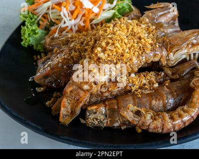 Frittierte Flusskrebse mit Knoblauch auf dem schwarzen Gericht serviert mit Gemüse auf dem Tisch, asiatische köstliche Meeresfrüchte. Gebratene Flusskrebse oder Gottesanbeterin umrühren Stockfoto