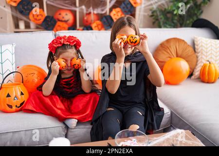 Ein süßer Junge und ein Mädchen, die halloween-Kostüme tragen und zu Hause Kürbiskörbe über die Augen halten Stockfoto