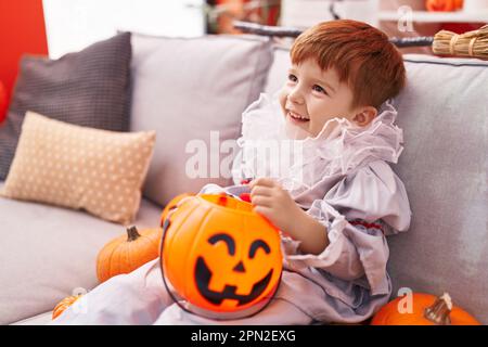 Ein niedliches Kleinkind, das zu Hause ein Harlequin-Kostüm trägt und einen Kürbiskorb hält Stockfoto