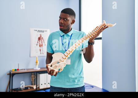 Ein afroamerikanischer Mann hält ein anatomisches Modell der Wirbelsäule im Schockgesicht, sieht skeptisch und sarkastisch aus, überrascht von offenem Mund Stockfoto