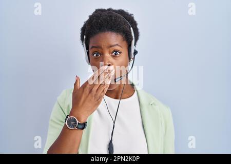 Eine afroamerikanische Frau, die ein Headset für Callcenter-Agenten trägt und den Mund wegen eines Fehlers mit Händen verdeckt. Geheimes Konzept. Stockfoto