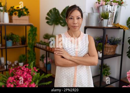 Junge asiatische Blumenfrau, die selbstbewusst im Blumenladen lächelt, mit gedrückten Armen steht Stockfoto