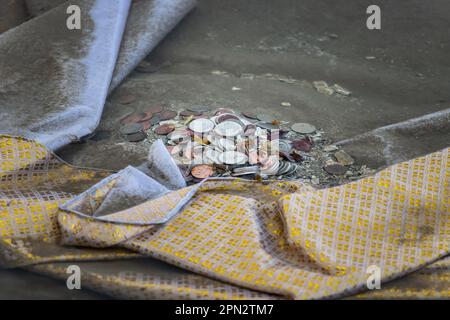 Ein Dekorationsstoff mit Münzen im Wasser an der Küste, Nahaufnahme. Ein Relikt des buddhistischen Bestattungsrituals in Bangkok, Thailand. Stockfoto