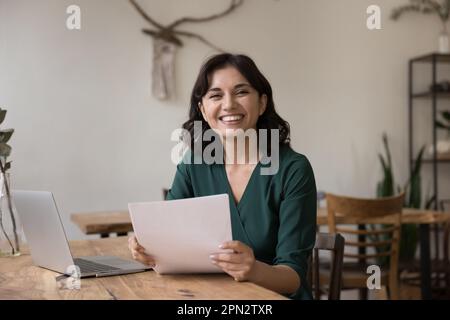 Glückliche junge armenische Geschäftsfrau sitzt am Schreibtisch und erledigt Papierkram Stockfoto