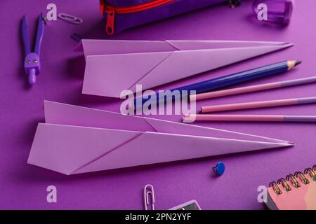 Komposition mit Schreibwaren und Papierflugzeugen auf violettem Hintergrund Stockfoto