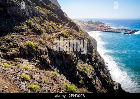 Nervenkitzel einer riskanten Wanderung auf einem schmalen Wanderweg entlang der zerklüfteten Klippen von Acantilados de Los Gigantes mit dem Hafen von Puerto de Los Gigantes. Stockfoto