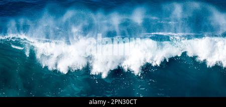 In diesem atemberaubenden Luftfoto wird eine gewaltige, stürzende Welle des Ozeans festgehalten, wobei die massive Welle in ein weißes Sprühnebel gegen das Wasser zerbricht. Stockfoto