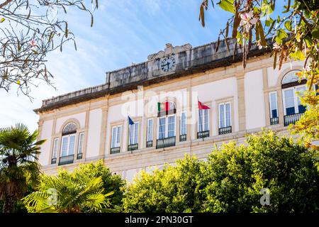 Die Fassade im ersten Stock des Rathauses von Câmara Municipal de Silves, geschmückt mit einer flatternden portugiesischen Flagge, steht hoch inmitten üppigen Grüns auf dem Stadtplatz Stockfoto