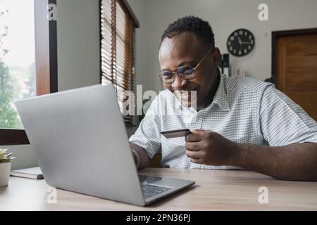 Kurze Aufnahme eines afroamerikanischen Geschäftsmanns, der online mit Kreditkarte bezahlt und Bestellungen über das Internet tätigt. Erfolgreicher schwarzer Mann hält Plastikkarte Stockfoto