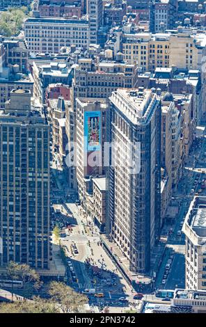 Das Flatiron Building, eine Ikone von New York City, wird durch den Dunst eines anderen Ikons, des Empire State Building, betrachtet. Renovierungsgerüste verdecken die Fassade. Stockfoto