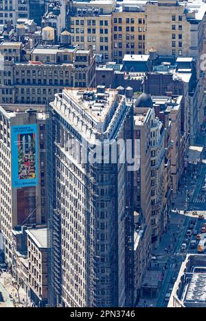 Das Flatiron Building, eine Ikone von New York City, wird durch den Dunst eines anderen Ikons, des Empire State Building, betrachtet. Renovierungsgerüste verdecken die Fassade. Stockfoto