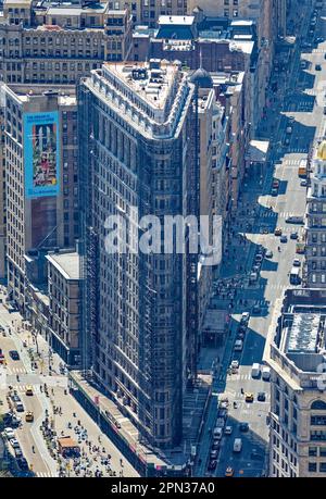 Das Flatiron Building, eine Ikone von New York City, wird durch den Dunst eines anderen Ikons, des Empire State Building, betrachtet. Renovierungsgerüste verdecken die Fassade. Stockfoto