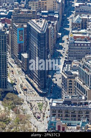 Das Flatiron Building, eine Ikone von New York City, wird durch den Dunst eines anderen Ikons, des Empire State Building, betrachtet. Renovierungsgerüste verdecken die Fassade. Stockfoto