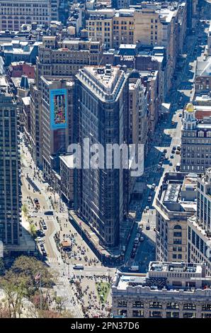 Das Flatiron Building, eine Ikone von New York City, wird durch den Dunst eines anderen Ikons, des Empire State Building, betrachtet. Renovierungsgerüste verdecken die Fassade. Stockfoto