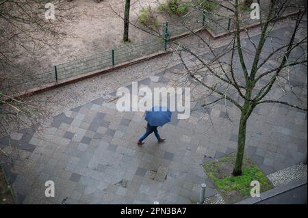 16.04.2023, Berlin, Deutschland, Europa - Person mit Schirm wandert im April im Bezirk Charlottenburg auf nassem Bürgersteig im Regen. Stockfoto