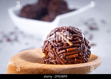 Die „Brigadier“-Süßigkeiten werden in einem Holzlöffel mit mehreren „brigadeiro“-Süßigkeiten auf einer weißen Schüssel hergestellt, auf dem Schokoladenstreusel liegen. Video schließen Stockfoto