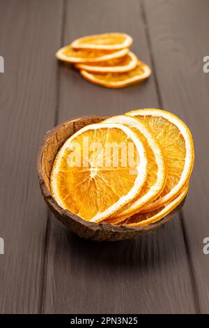 Orangenchips in einer Kokosnussschale. Scheiben getrockneter Orangen auf dem Tisch. Draufsicht. Dunkler Holzhintergrund. Stockfoto