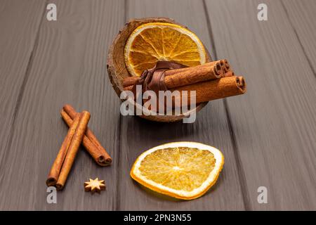 Zimtstangen in einem Haufen und Orangenchips in einer Kokosnussschale. Zimtstangen auf dem Tisch. Dunkler Holzhintergrund. Stockfoto