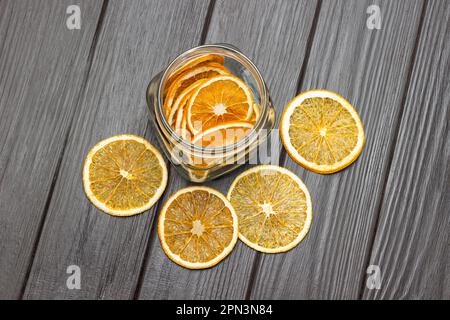 Trocknen Sie die orangefarbenen Scheiben auf dem Tisch und in einem Glas. Flach verlegt. Speicherplatz kopieren. Dunkler Holzhintergrund. Stockfoto