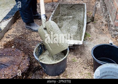 Der Arbeiter legt Beton in einen Eimer mit Schaufel im Garten im Freien des Dorfes Stockfoto