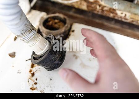 Klempnerhand in der Nähe des Kanalisationsrohrs und gewellter Ablaufschlauch in der Nähe des alten Dorfhauses Stockfoto