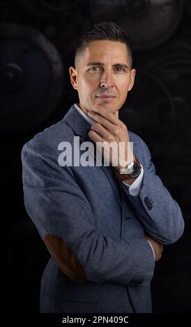 Ein gutaussehender, selbstbewusster Geschäftsmann im Anzug, der über dunklem Hintergrund steht Stockfoto