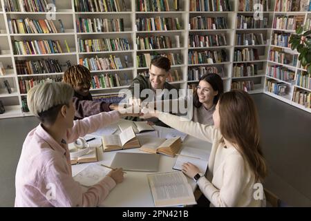 Fünf fröhliche Schüler feiern den erfolgreichen Abschluss der Prüfung in der Bibliothek Stockfoto