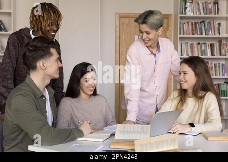 Fünf verschiedene Teenager-Schüler, die Teamarbeit leisten, treffen sich in der Bibliothek Stockfoto