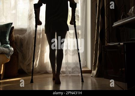 Ein kleines Mädchen mit Krücken geht ins Schlafzimmer in ihrer Wohnung, in der Nähe des Fensters, Rehabilitation Stockfoto