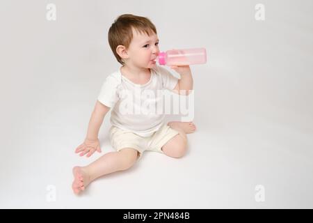 Happy Baby trinkt Milch aus der Flasche auf weißem Studiohintergrund. Ruhendes Kind isst Formel. Kind etwa zwei Jahre alt (ein Jahr neun Monate) Stockfoto