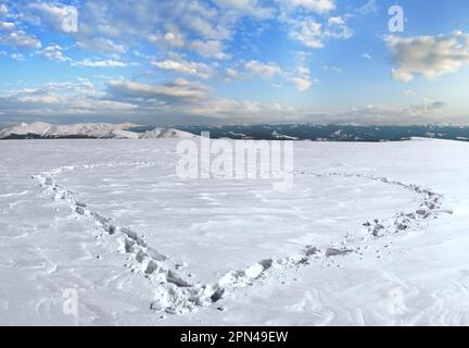 Menschlichen Fußabdruck bilden die Herzform auf schneebedeckten Berg-Plateau und Bergketten hinter. Stockfoto