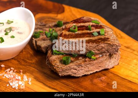 Rumpsteak auf einem Holzbrett mit Pilzsauce. Hochwertiges Rindfleisch. Grillsaison. Mittelgroßes gegrilltes Steak. Stockfoto